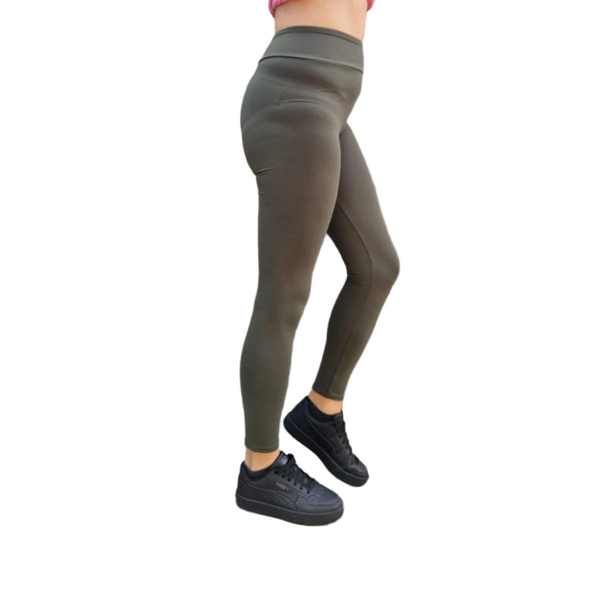 Person wearing pink top and green leggings standing against a wooden wall.