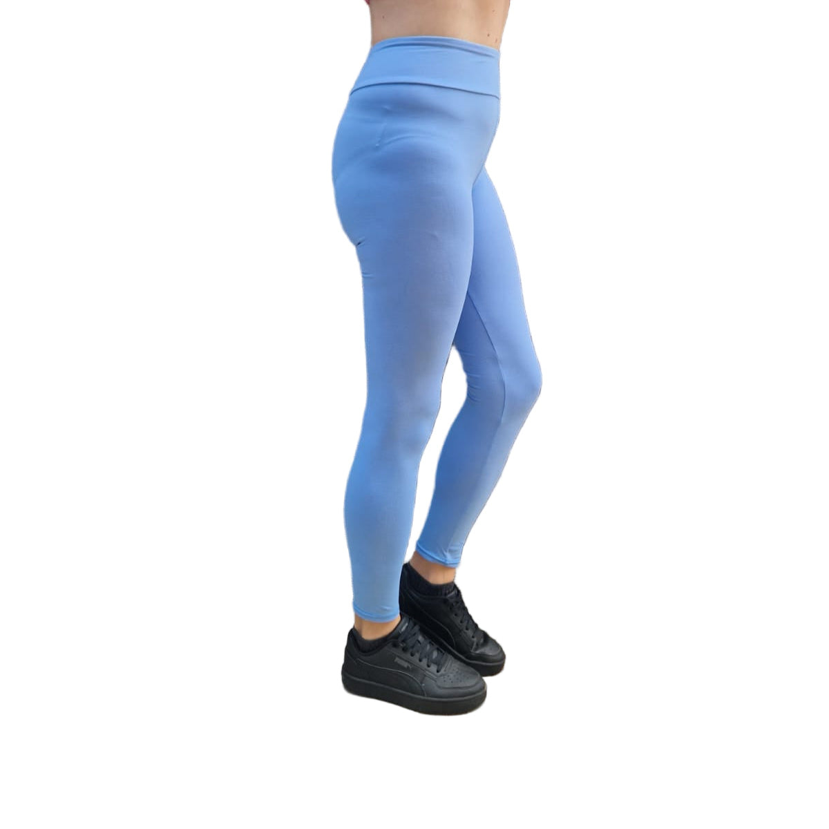 Person wearing pink top and blue leggings standing against a wooden wall.